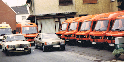 Ein altes Foto vom Fuhrpark der Auto Bachem GmbH. Sieben Busse und zwei Mercedes-Taxis stehen geparkt auf dem Firmengelände.