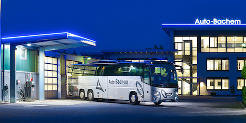 Ein Reisebus steht auf dem Firmengelände der Auto Bachem GmbH. Das Firmengebäude im Hintergrund ist beleuchtet.